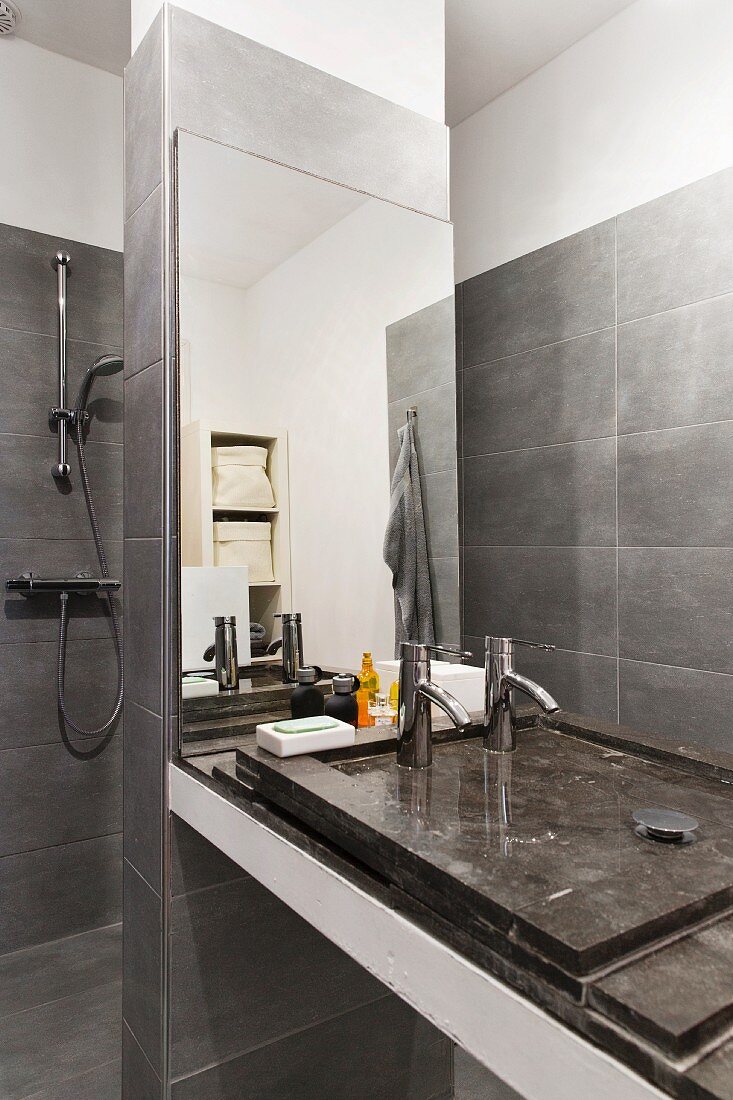 Grey-tiled designer bathroom with minimalist washstand on mirrored partition screening shower