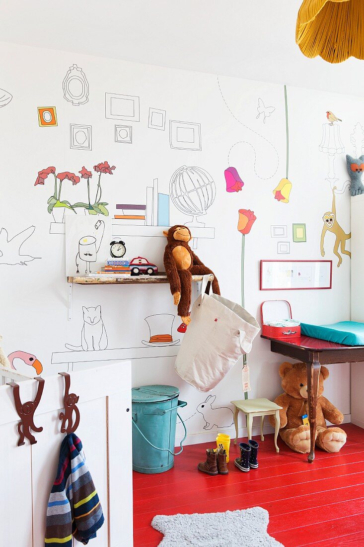 Stofftiere auf Wandbord und unter dem Tisch auf rot lackiertem Dielenboden im Kinderzimmer