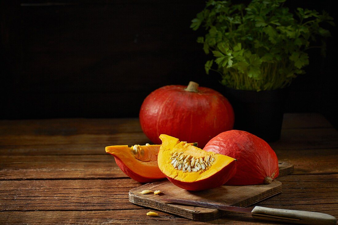 Orange pumpkins, whole and sliced, on a chopping board with a knife