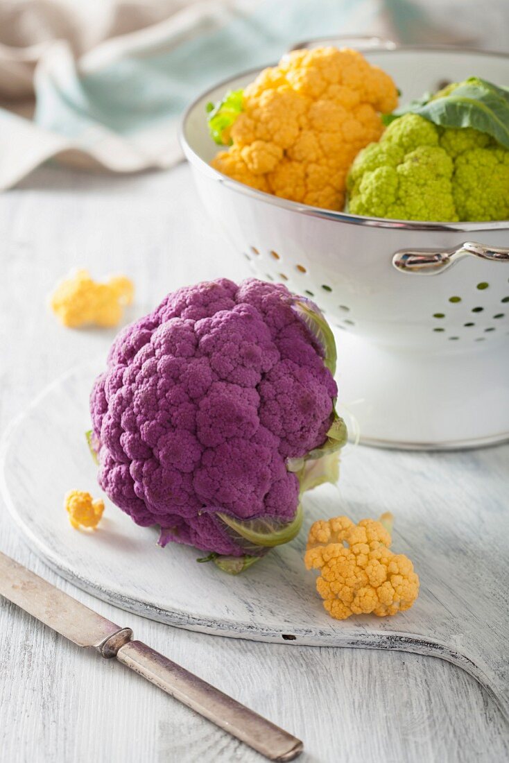 Different coloured cauliflower in a colander and on a chopping board