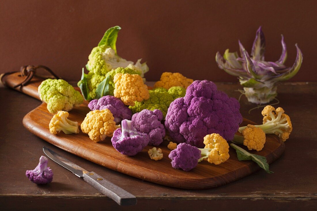 Various different coloured types of cauliflower on a chopping board