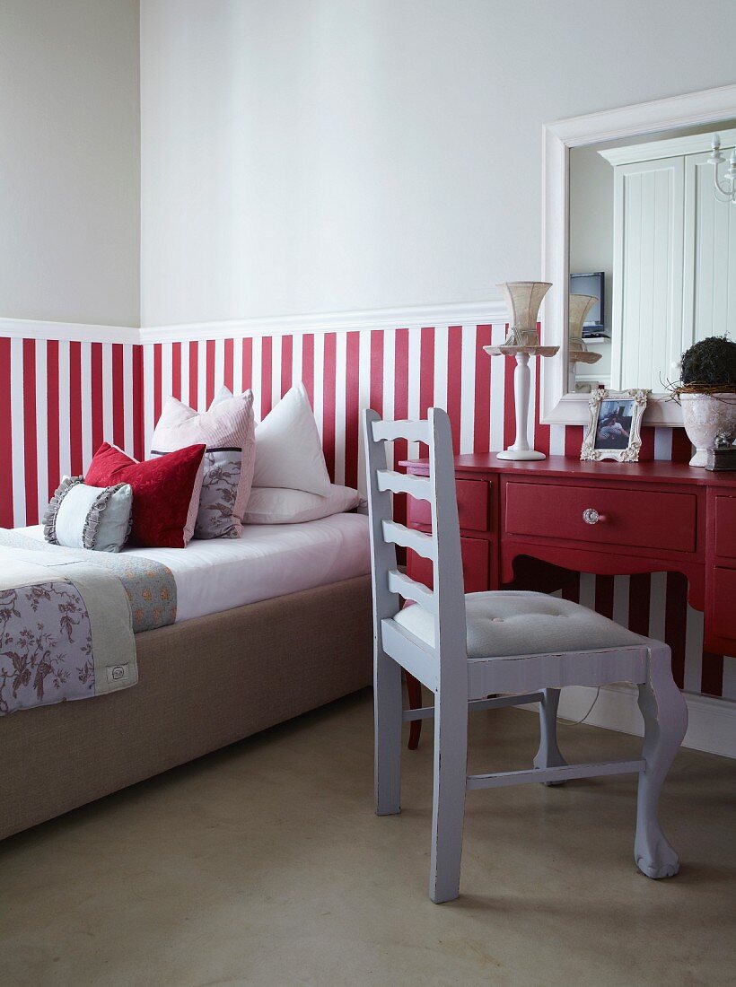 Chair painted pale grey in front of red desk next to bed in bedroom with red and white striped dado