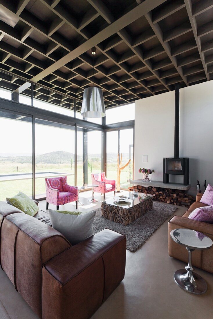 Leather sofa set and pink armchairs around block-style coffee table next to glass wall with view of landscape
