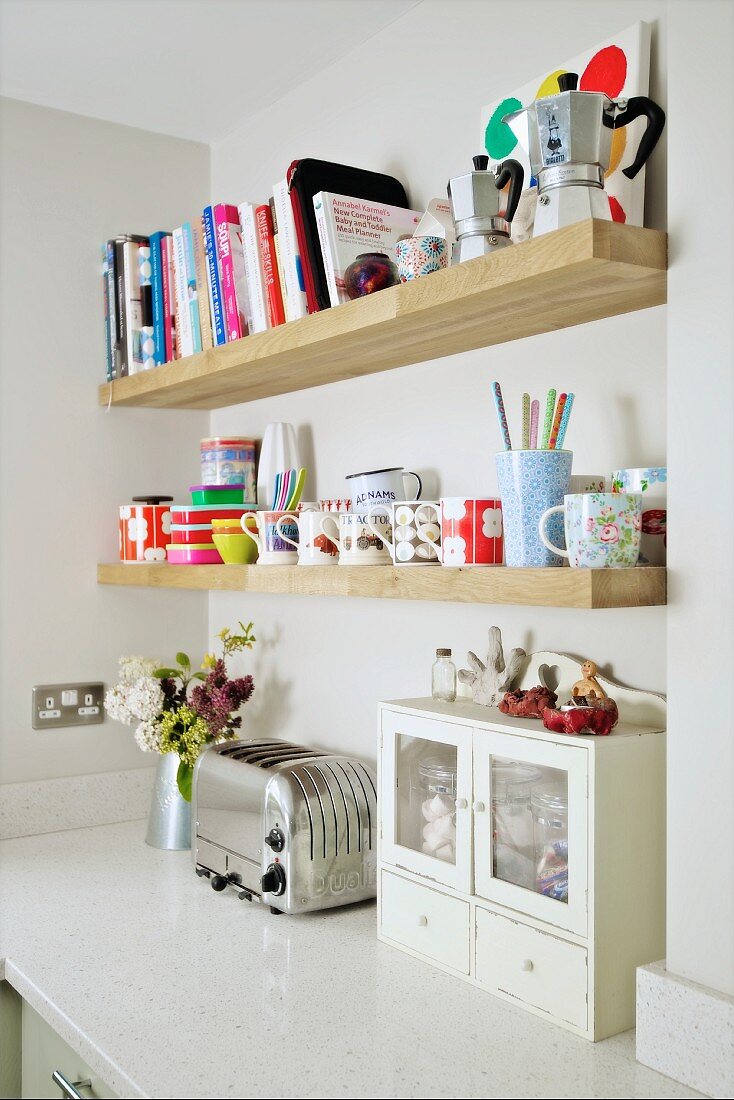 Wooden shelves of books and crockery on wall above retro toaster on kitchen counter