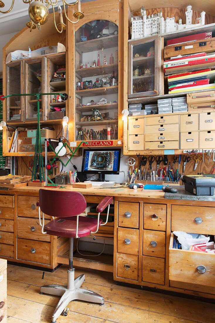 Workshop ambiance - vintage swivel chair in front of desk with drawers and tools hanging under wall-mounted cabinets