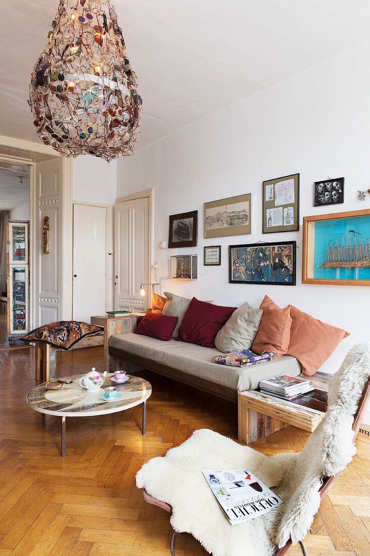 Easy chair with sheepskin blanket, couch and coffee table below chandelier made from metal and old spectacles