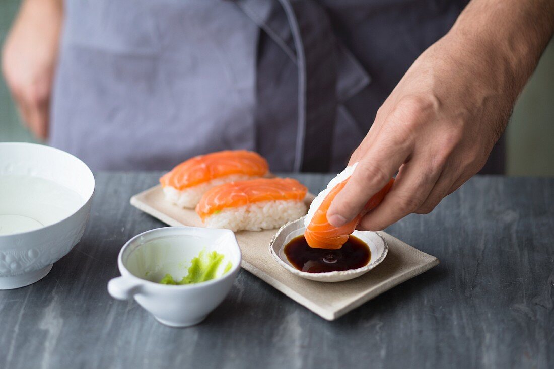 Nigiri sushi with salmon being dipped in soy sauce and wasabi paste