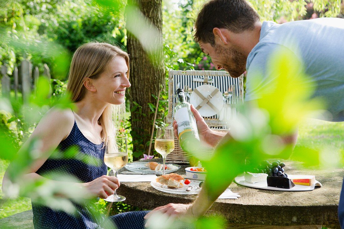 A couple drinking white wine with a picnic in a garden
