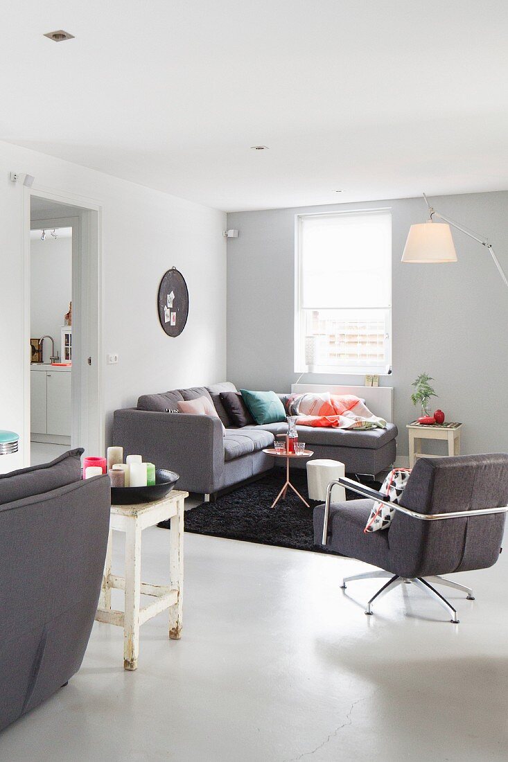 Grey swivel armchair and corner couch in lounge area with designer standard lamp