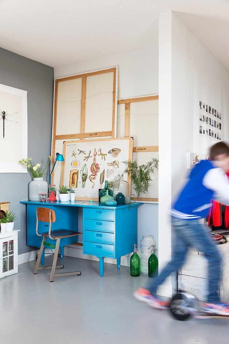 Blue-painted desk and retro chair in niche; child riding by on scooter