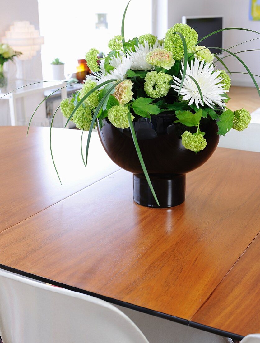 Hydrangeas and white dahlias in black designer vase on wooden table