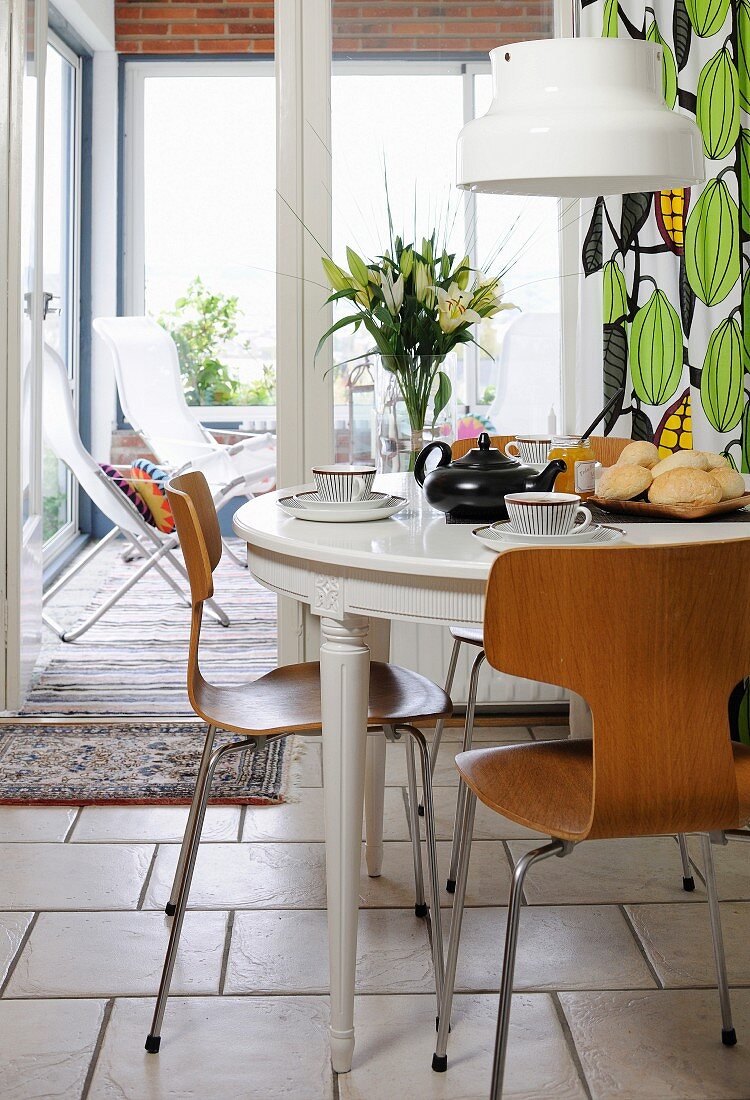 Round breakfast table with Scandinavian laminate-wood chairs and view into conservatory in background