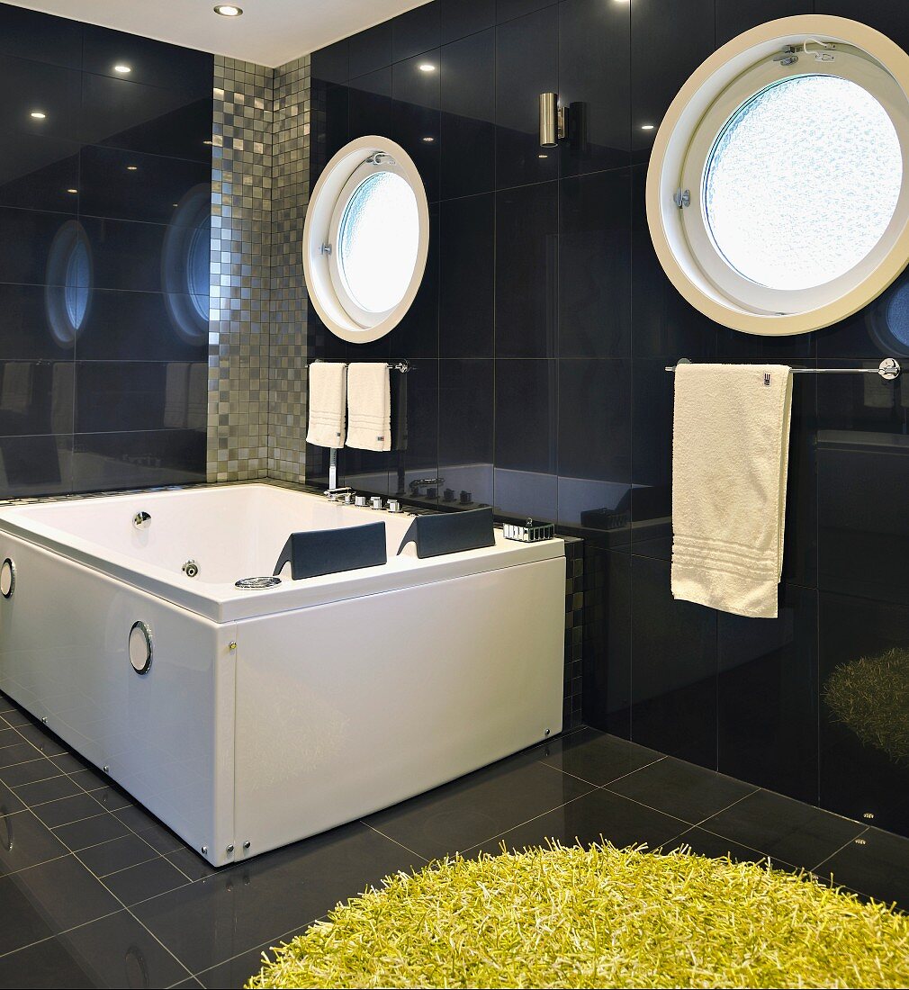 Porthole window above whirlpool in dark-tiled bathroom