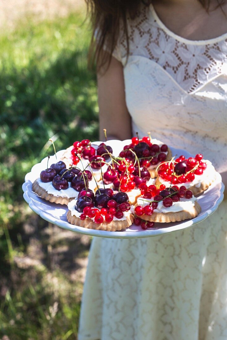 A little girl holding a plate of cherry and redcurrant tartlets