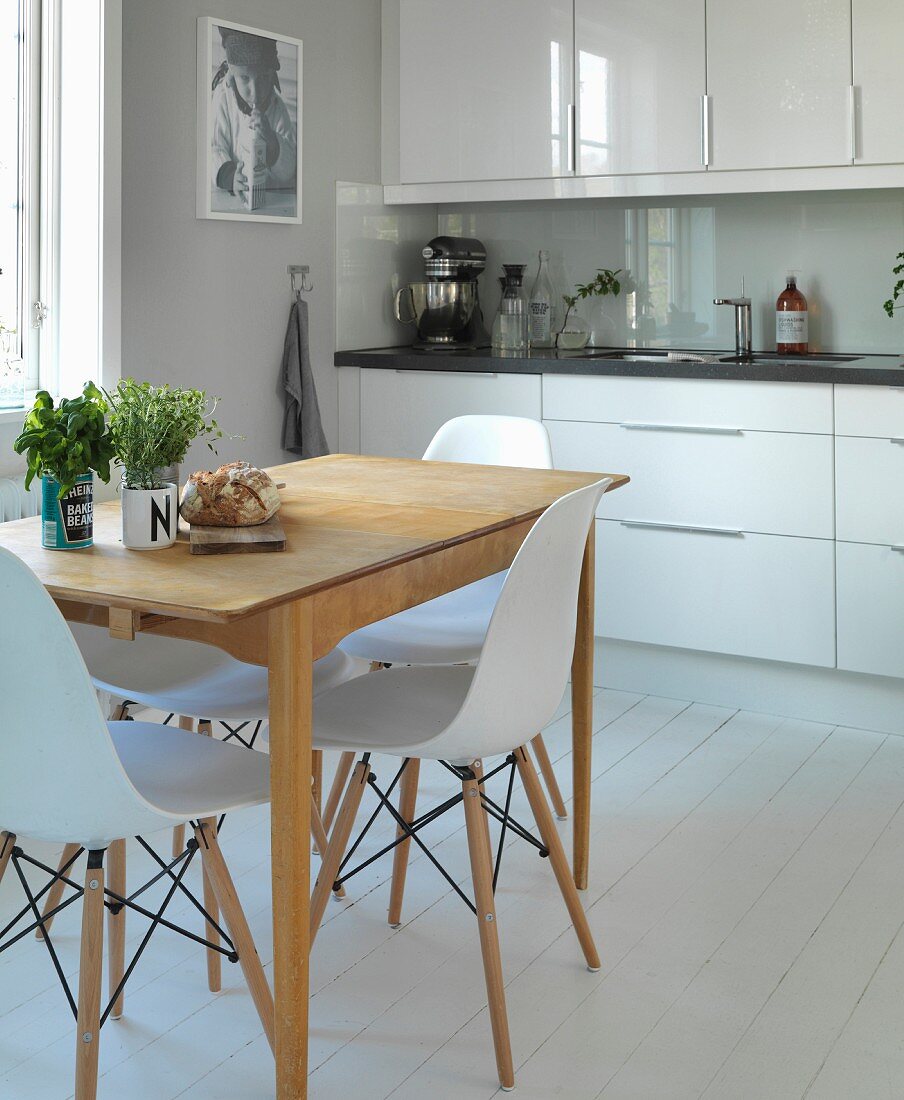 Elegante weiße Küchenzeile mit Vintage-Küchentisch und Eames-Stühlen in renoviertem Landhaus