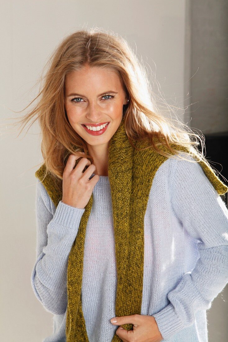 A young blonde woman wearing a light knitted jumper with a green jumper over her shoulders