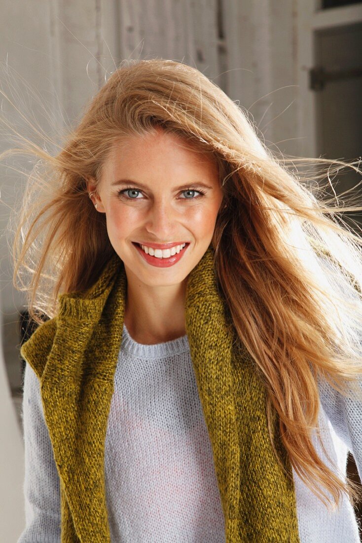 A young blonde woman wearing a light knitted jumper with a green jumper over her shoulders