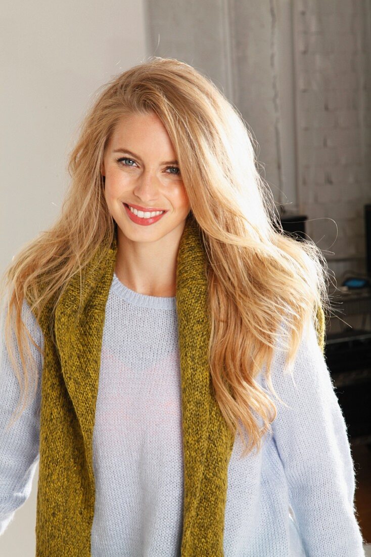 A young blonde woman wearing a light knitted jumper with a green jumper over her shoulders