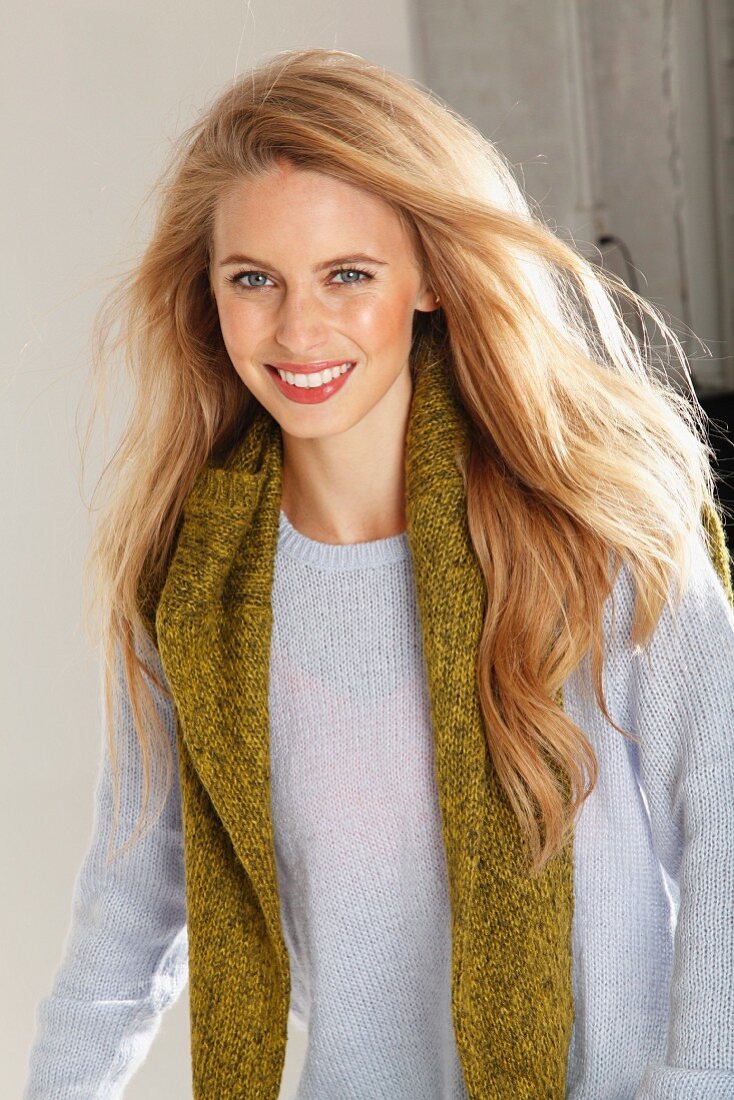 A young blonde woman wearing a light knitted jumper with a green jumper over her shoulders