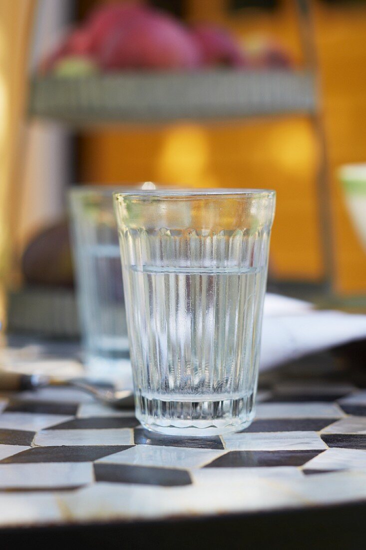 A glass of water on a French bistro table with a black and white diamond pattern