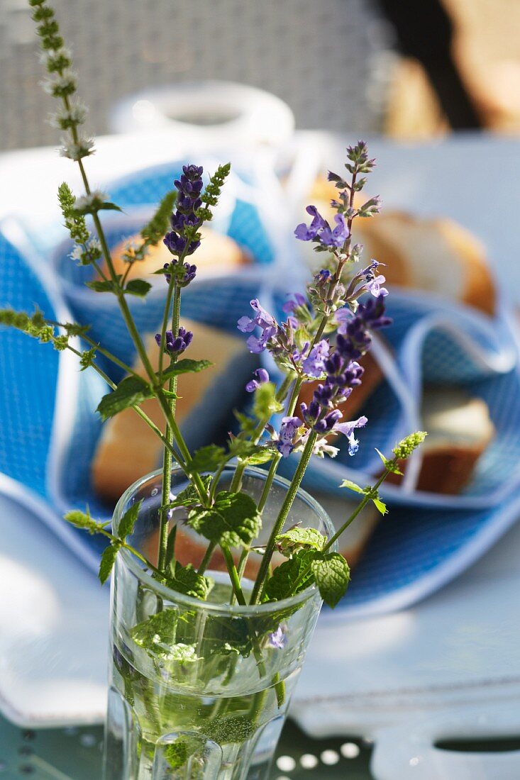 Lavender flowers and mint in a glass with an out of focus baguette basket in the background