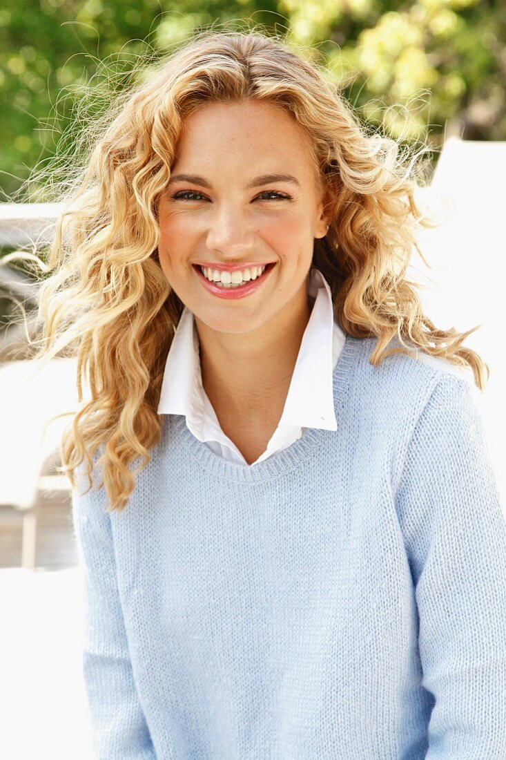 A young blonde woman outside wearing a white shirt and a light blue knitted jumper