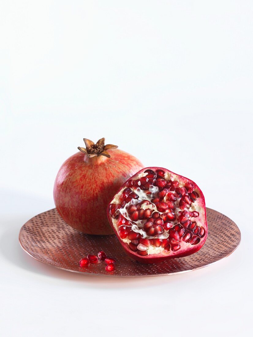 A whole and a halved pomegranate on a copper plate