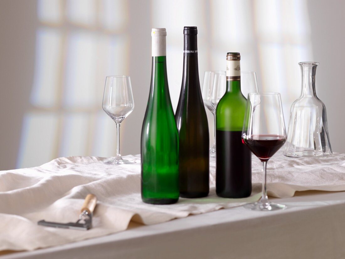 Rotweinglas, Weinflaschen und leere Gläser
