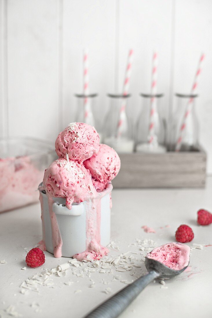 Frozen raspberry yogurt with grated white chocolate in a pot with mini bottles of milk in the background