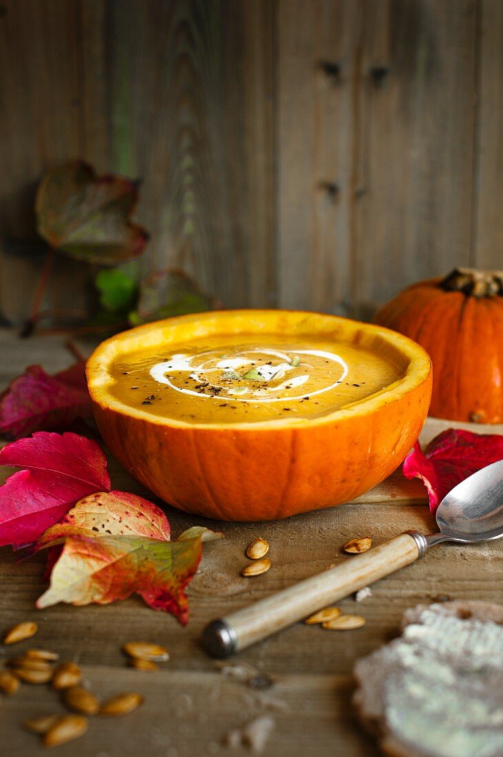 Autumnal pumpkin soup served in a hollowed out pumpkin with sour cream and pumpkin seeds