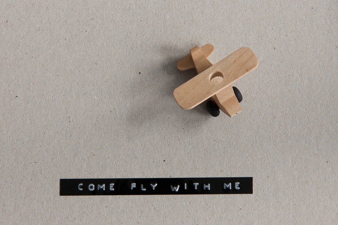 Wooden toy plane and adhesive tape from label maker reading -COME FLY WITH ME-