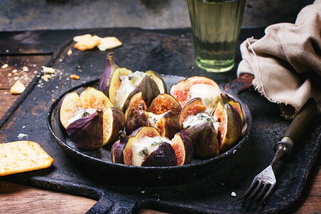 Figs filled with blue cheese in an old pan served with crackers and a glass of white wine