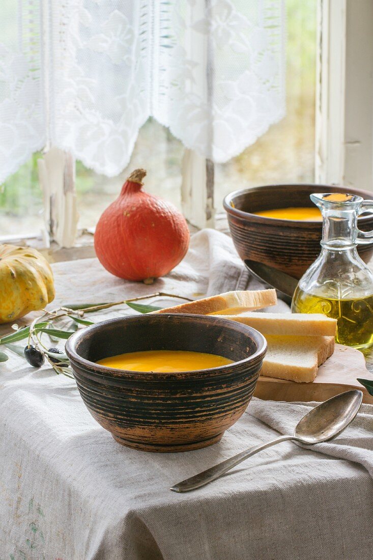 Lunch with pumpkin soup and green olives, served on an old wooden table by a window
