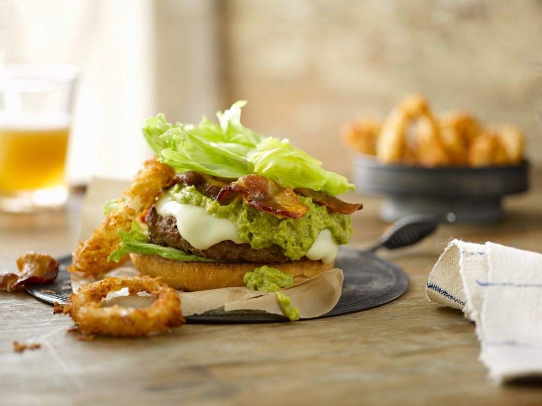 A cheeseburger with cheddar, guacamole, bacon, iceberg lettuce and crispy onion rings