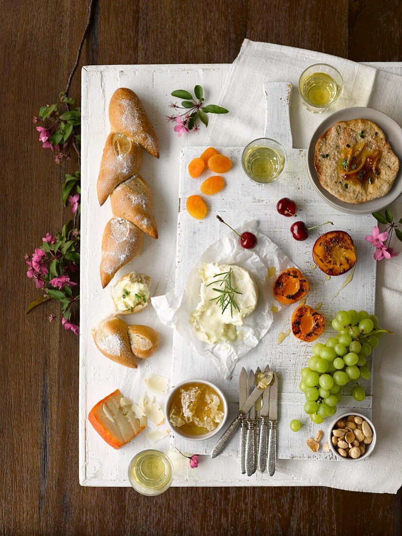 An appetiser platter featuring grilled peaches, apricots, cherries, grapes, nuts, honeycomb, bread and white wine