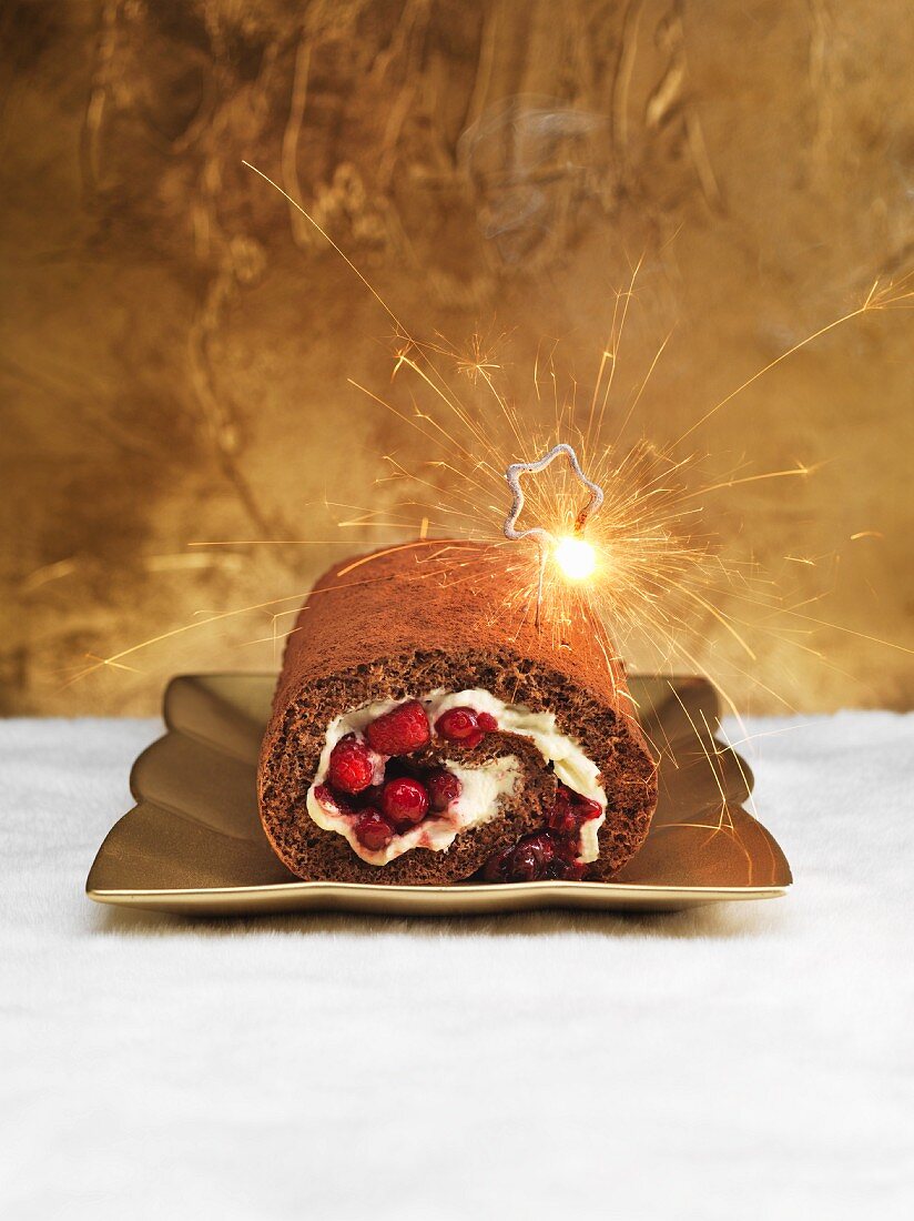 A chocolate Swiss roll with berries and a sparkler for Christmas