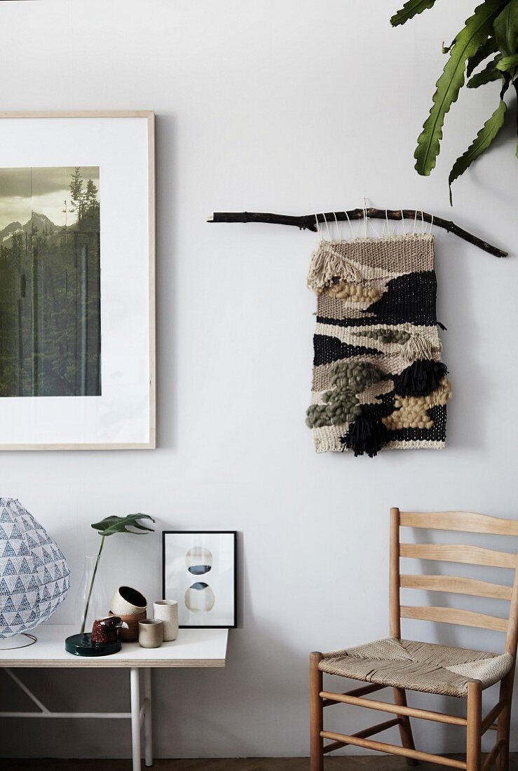 Hand-woven wall hanging in natural shades above rush-bottom chair next to ornaments on table