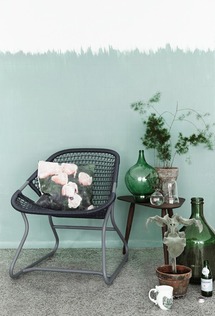Hand-crafted cushion cover with photo print on tubular metal chair with woven seat next to collection of vintage bottles