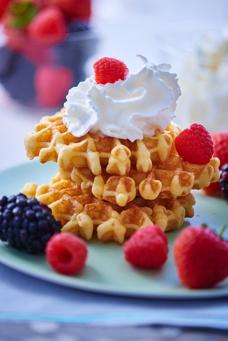 A stack of three fresh waffles topped with whipped cream and fresh berries