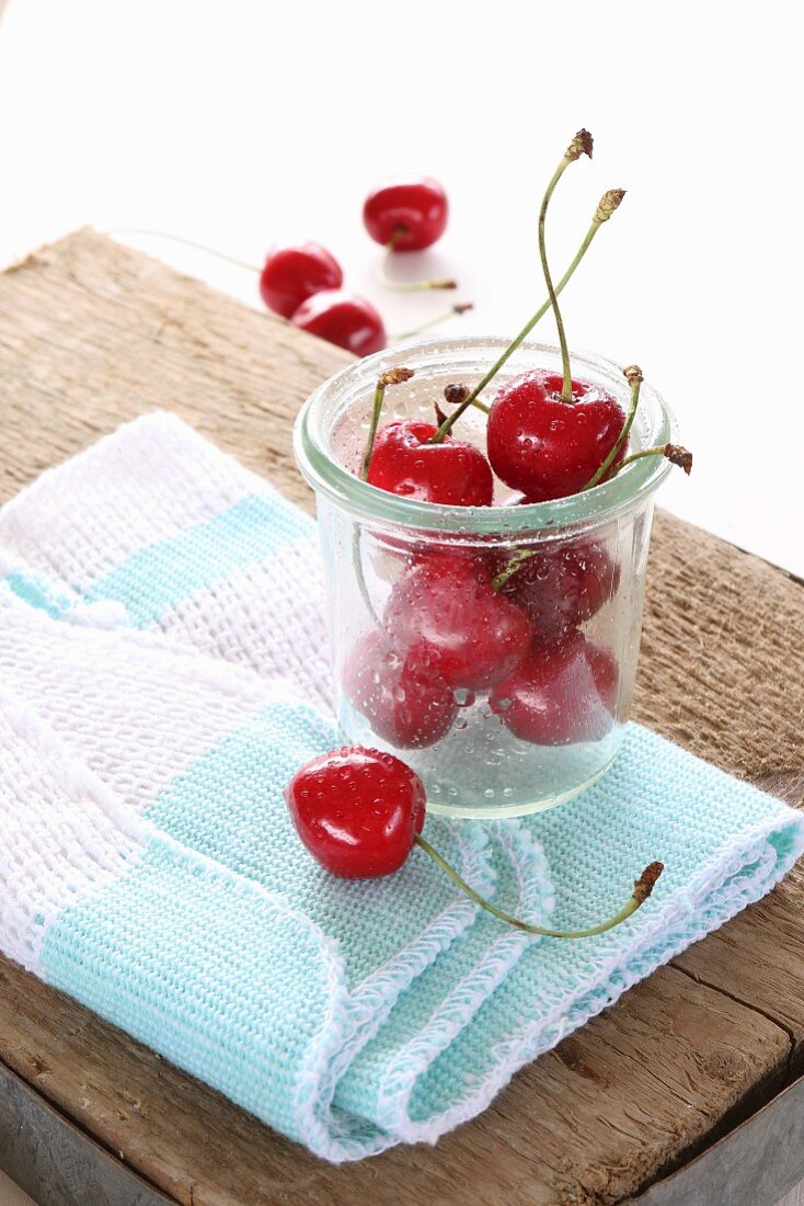 Fresh cherries with stems in a glass on a cloth on a rustic wooden board
