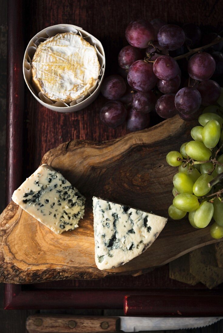 Various types of cheese and grapes on a wooden surface