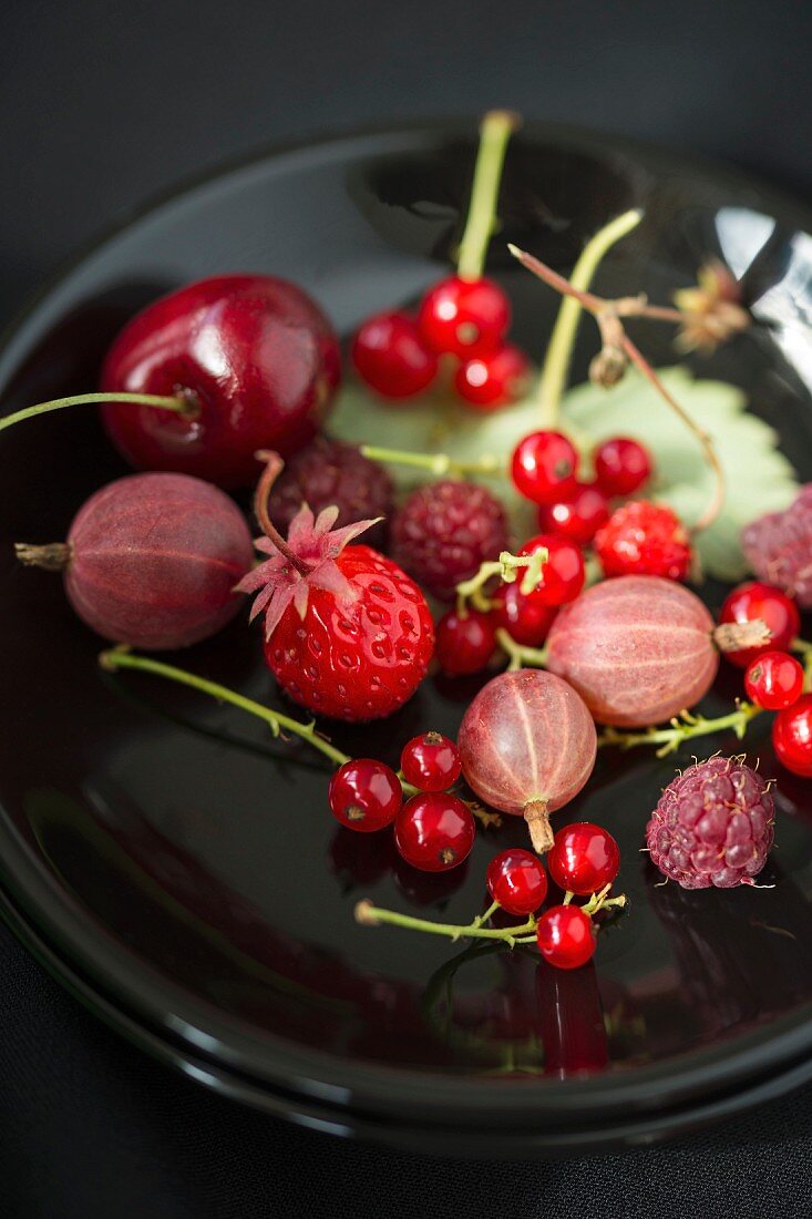 Various berries on a plate (redcurrant, gooseberries, raspberries, wild strawberries and cherries)