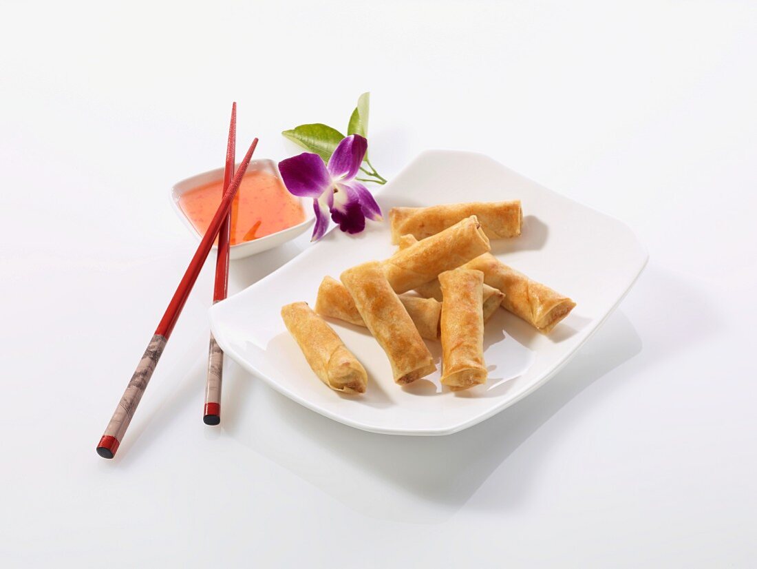 Spring rolls with chilli sauce, chopsticks and an orchid (China)