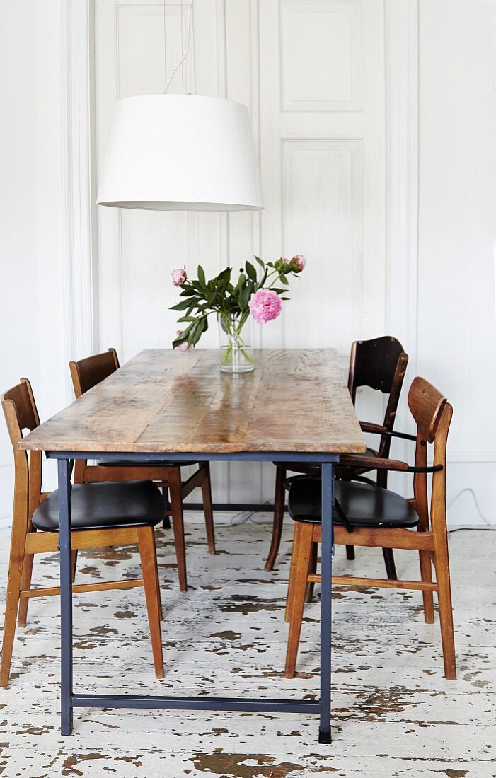 Rustikaler Tisch und Holzstühle im 60er Jahre Stil, darüber zeitgenössische Pendelleuchte mit weißem Schirm, im Esszimmer mit Holzdielenboden im Used Style