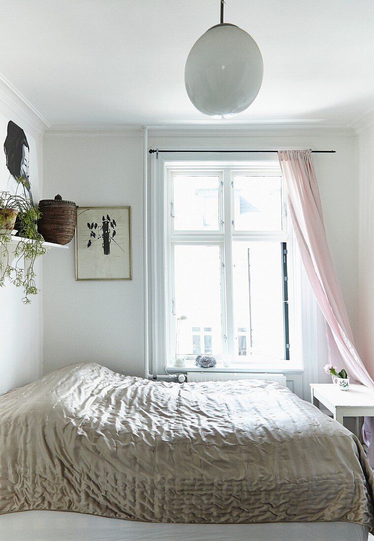 Double bed with shiny bedspread in front of window in white bedroom