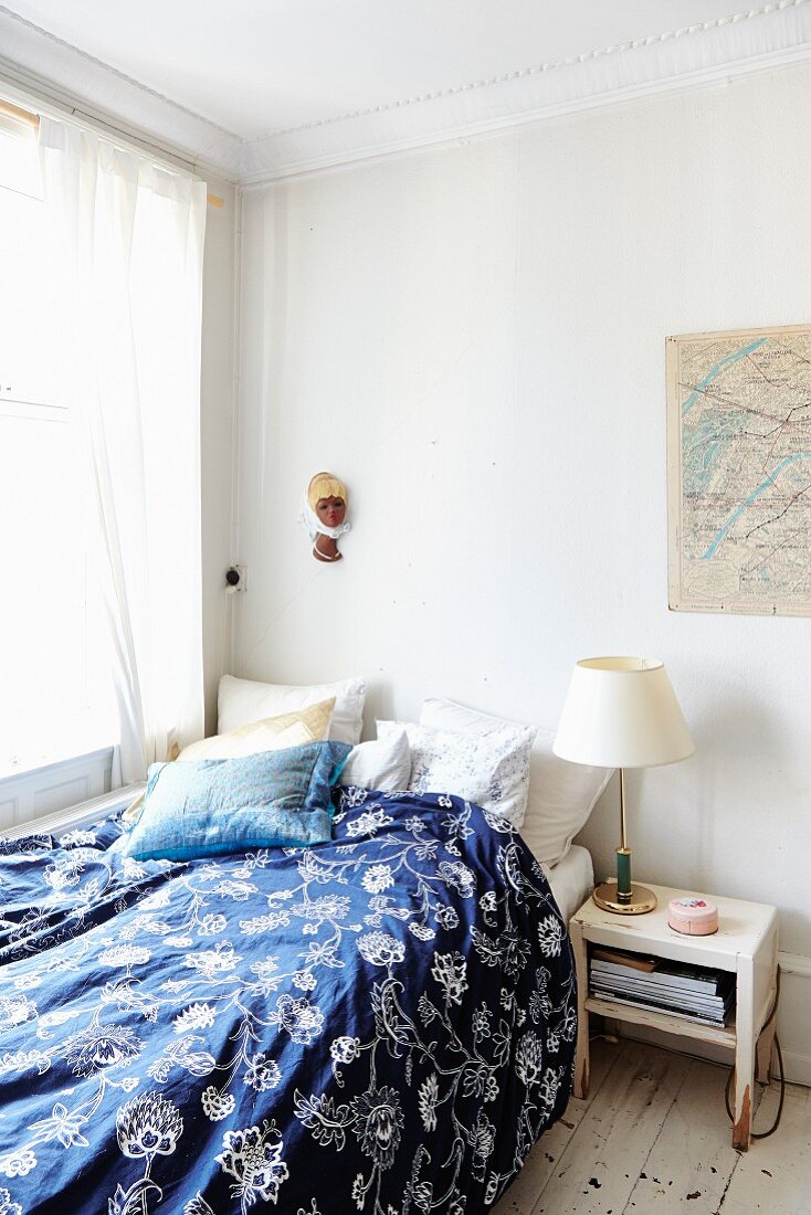 Bett mit blau-weiss gemusterter Bettwäsche, in schlichter Zimmerecke