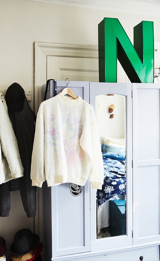 Jumper hanging on white-painted wardrobe with large, green ornamental letter on top