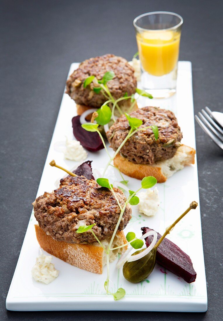 Mini burgers on slices of white bread with capers and beetroot