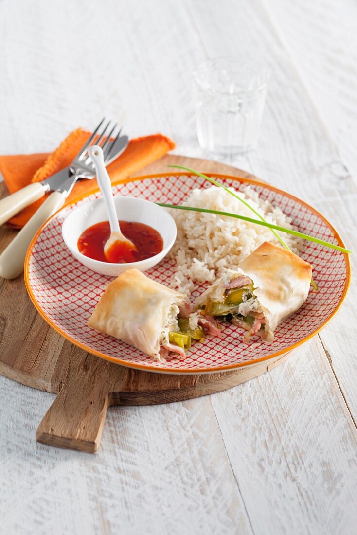 Puff pastry rolls filled with vegetables and ham served with rice and chilli sauce