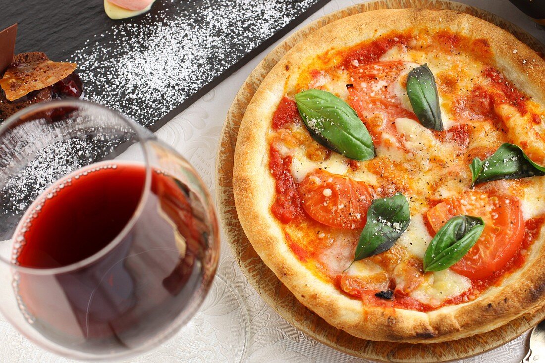 Pizza Napoli with tomatoes, cheese and basil served with a glass of red wine